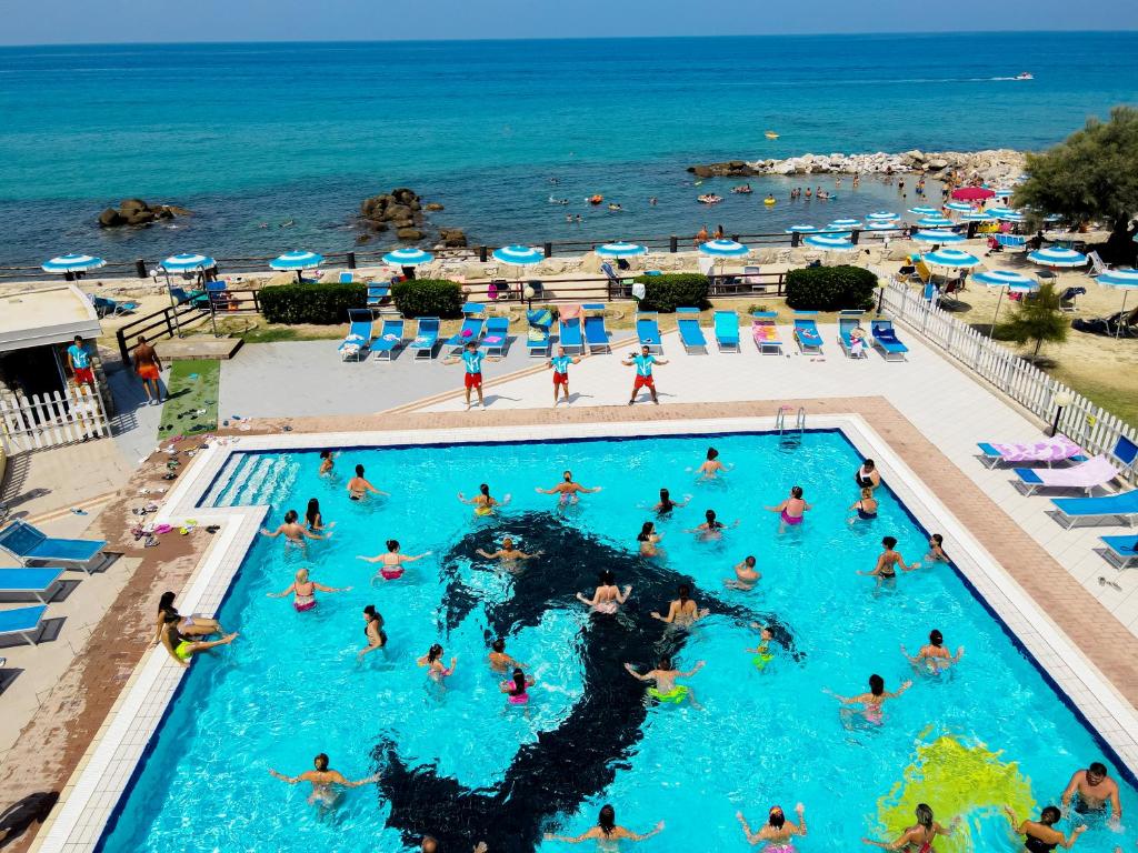 Peldbaseins ar daudziem cilvēkiem, kas izbauda ūdens aktivitātes, un skaista pludmale fona. Vasaras atmosfēra un relaksējoša vide.