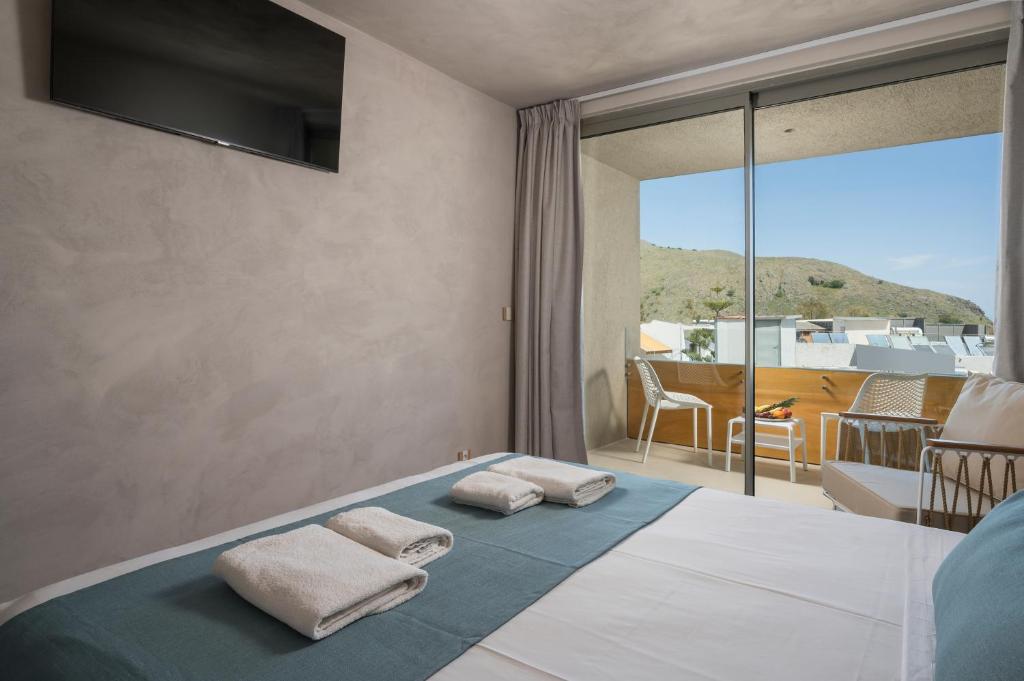 Mūsdienīga guļamistaba ar balkonu un skatu uz kalniem, kurā ir televizors un ērti gultas piederumi. Interjers ir gaišs un minimālistisks.