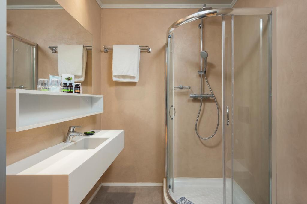 Mūsdienīgs vannas istabas interjers ar stikla dušu, baltu izlietni un brīvi plūstošām dvieļu turētājiem. Siltas krāsas un minimālisma dizains.