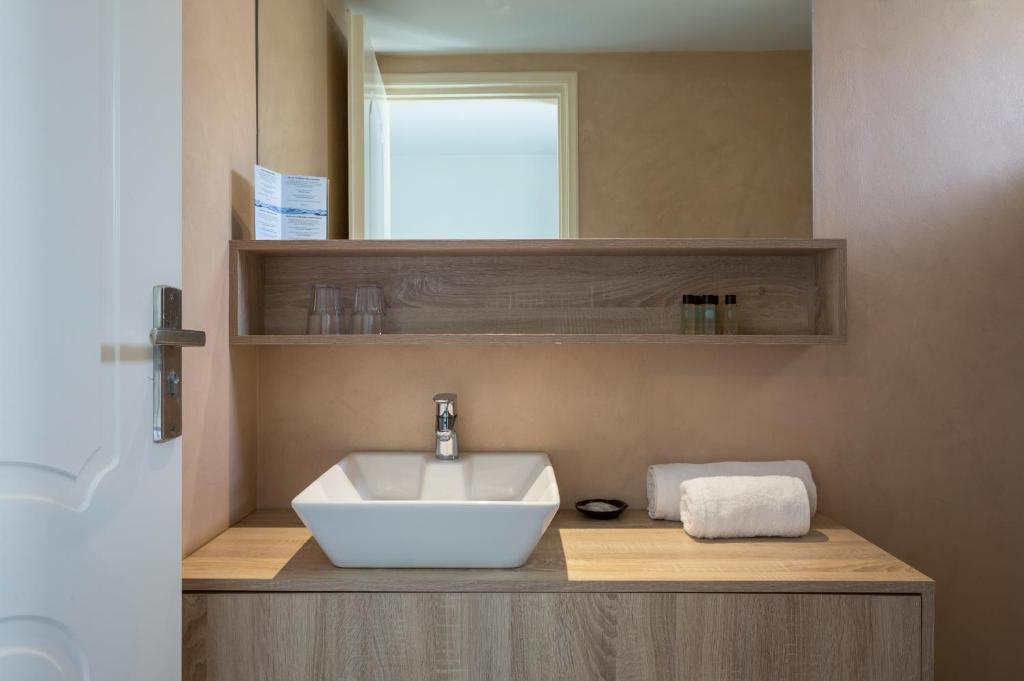 Mūsdienīgs vannas istabas interjers ar gaišu koka skapīti, balto izlietni un dvieli. Uz plaukta atrodas glāzes un higiēnas līdzekļi.