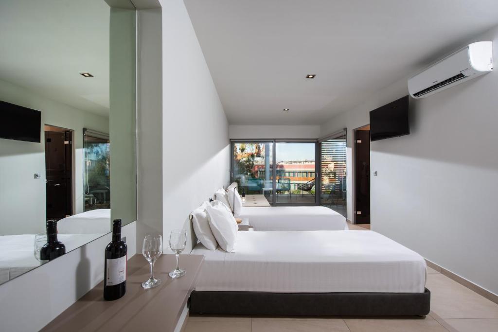 Mūsdienīgs viesnīcas numurs ar divām gultām, vīna pudeli un glāzēm, kā arī lieliem logiem, caur kuriem redzama terase un ainava.