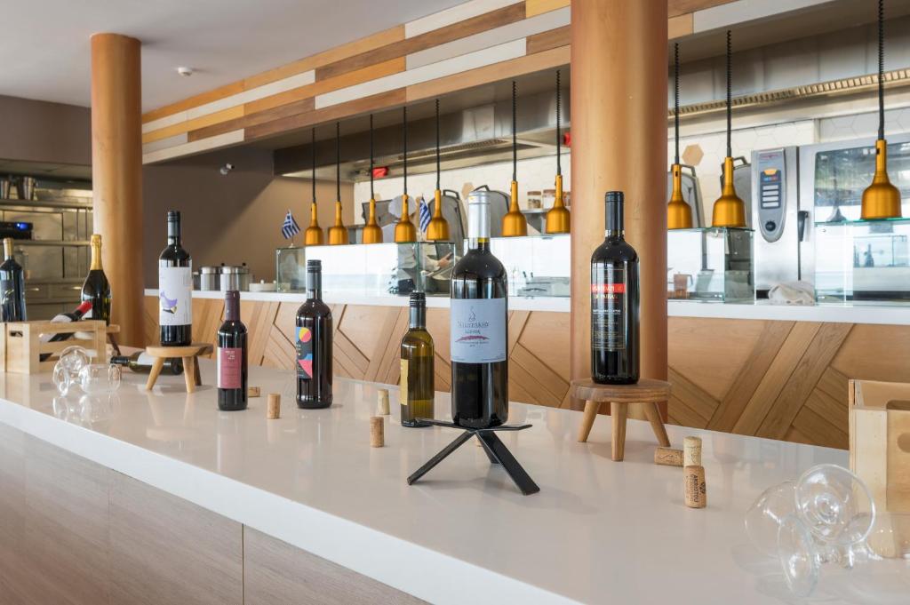 Vīna pudeļu izstāde modernā restorānā, kuras fons veido elegantus koka elementus un stilīgas apgaismojuma lampas. 