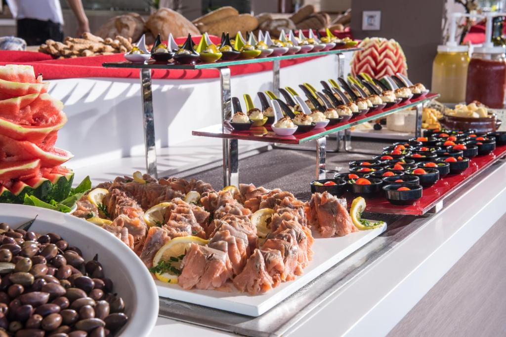 Pasaules virtuves bufete ar dažādiem ēdieniem, tostarp zivīm, augļiem un saldajiem našķiem, kas sakārtoti uz elegantām plauktiem.