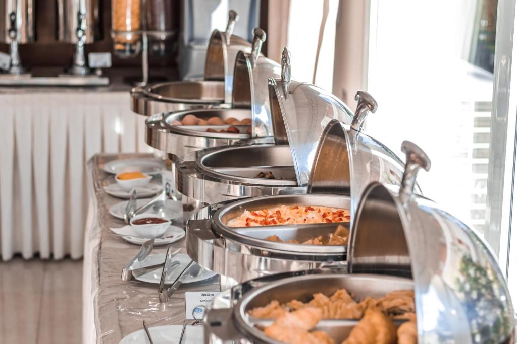 Pusdienu bufete ar dažādiem ēdieniem un saldumiem, ieskaitot olas, konditorejas izstrādājumus un mērces. Spīdīgas metāla trauki piepildīti ar gardumiem, gaidot viesus.