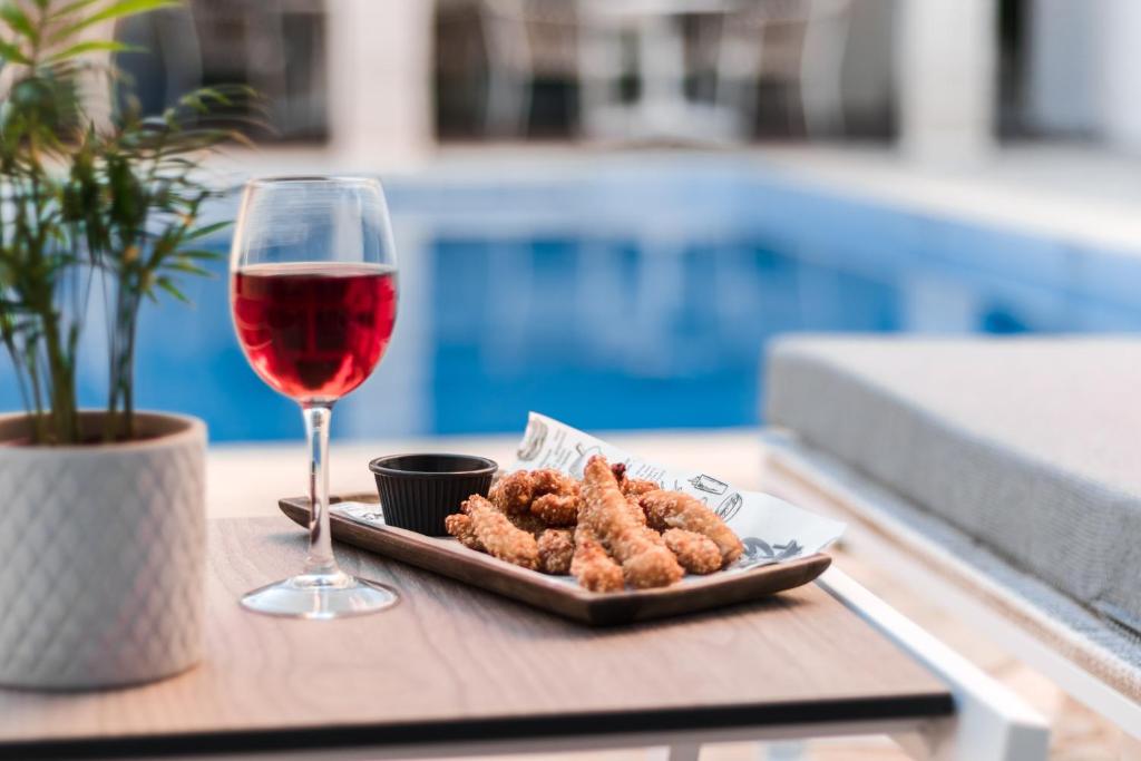 Sarkanais vīns un kraukšķīgi vistas gabaliņi uz galda blakus baseinam, radot relaksējošu atmosfēru. Ideāla vasaras atpūtas aina.
