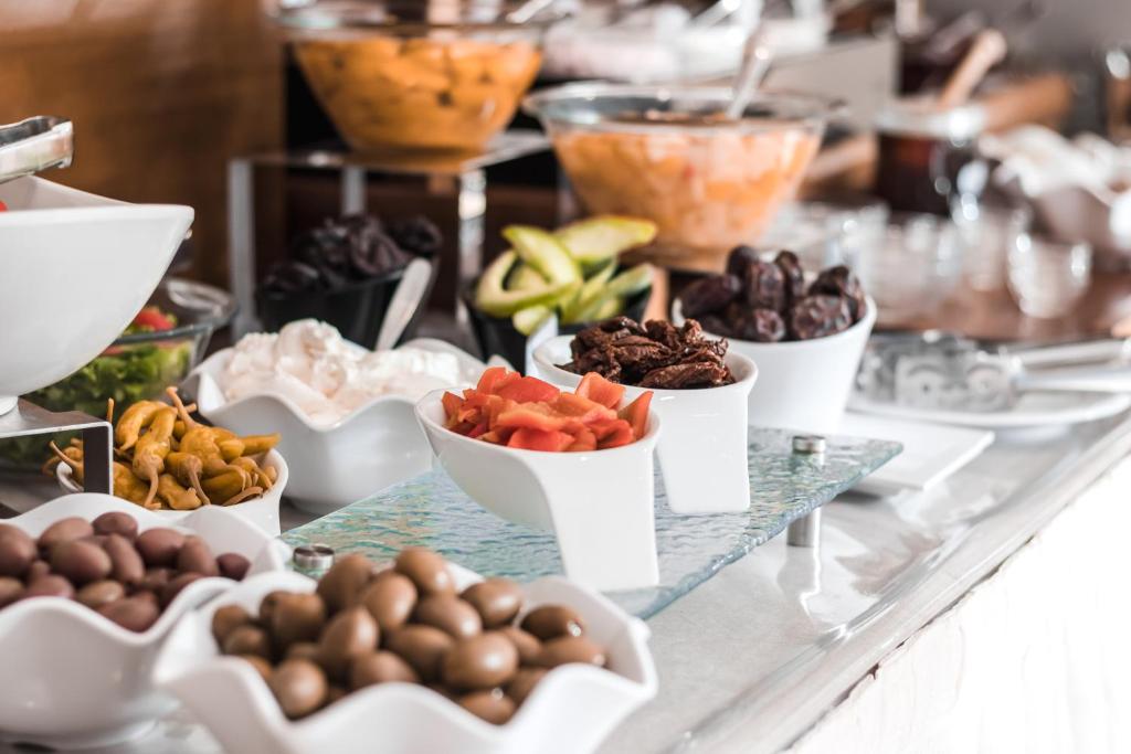 Dažādu uzkodu un salātu bufete ar dažādiem dārzeņiem, augļiem un garnējumiem, kas pasniegti baltā traukā.