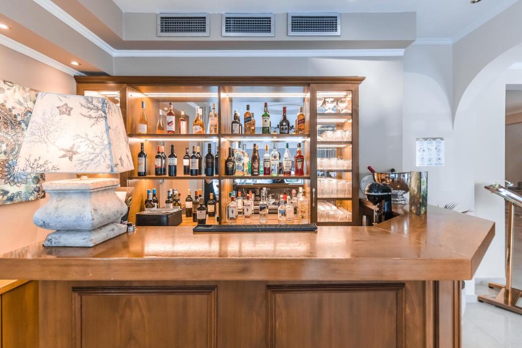 Koka bāra apmale ar stikla skapīti, kurā redzami dažādi dzērieni un glāzes, veido mājīgu atmosfēru. Uz bāra ir lampa un dekoratīvs attēls uz sienas.