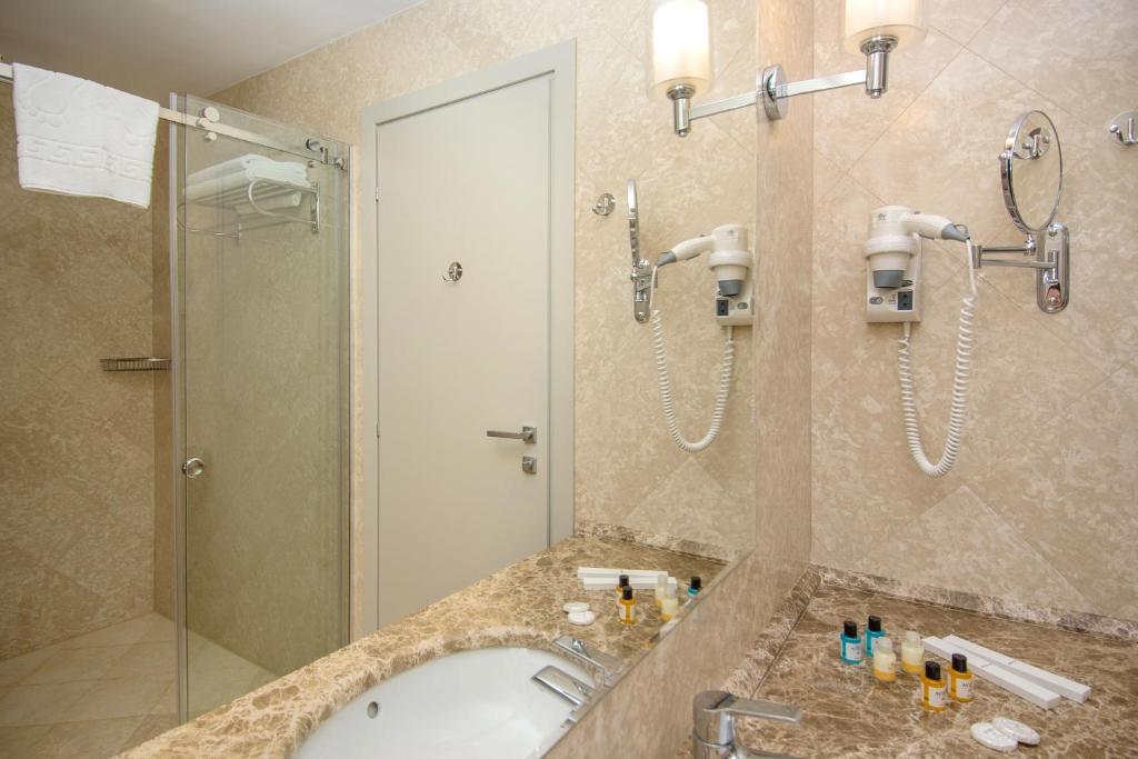 Mūsdienīga vannas istaba ar stikla dušu, marmora izlietni un aksesuāriem, kas ietver matu žāvētāju un kosmētikas produktus. Eleganta un funkcionāla telpa ar gaišām krāsām.