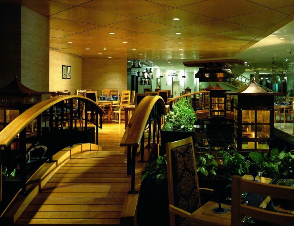 Mūsdienīgs restorāns ar koka tiltiņu, dekoratīvām gaismām un zaļajiem augiem, radot relaksējošu atmosfēru. Interjers apvieno eleganci un dabu.