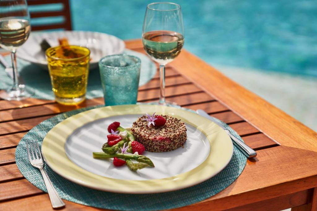 Grezns ēdiens uz galda pie baseina, rotāts ar avenes un ziediem, kopā ar glāzi baltvīna un dzirkstošām dzērienu glāzēm. Ideāla vasaras maltīte.