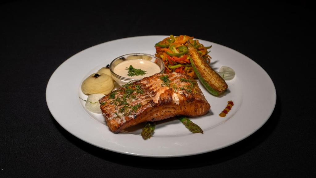 Garšīgs cepts lazis ar dārzeņu salātiem, krējuma mērci un garnelēm, pasniegts uz balta šķīvja.