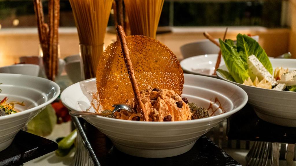 Saldais ēdiens ar kraukšķīgu cepumu un kafijas pupiņām, pasniegts elegantā traukā. Fonā redzami citi ēdieni un dekorācijas.