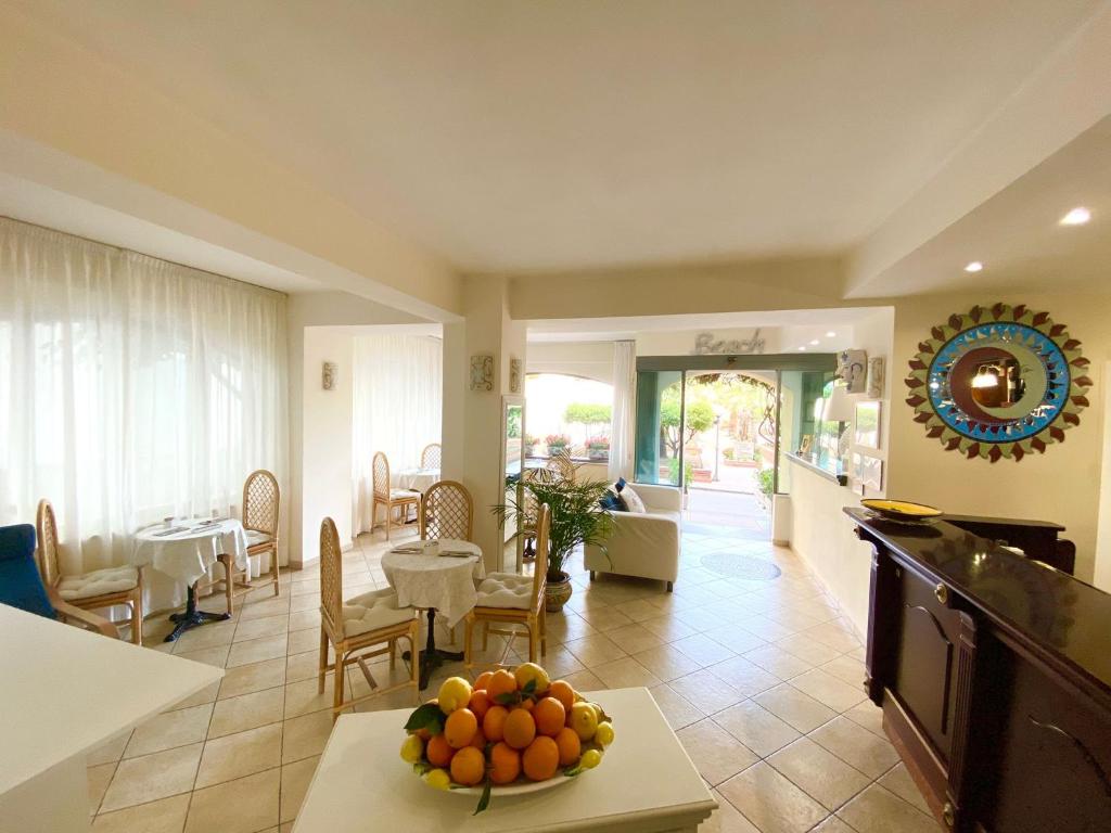 Gaišs un mājīgs interjers ar viesistabu, kurā redzami koka krēsli un galdi, kā arī augļu trauks centrā. Iespēja redzēt dārzu caur lielajiem logiem.