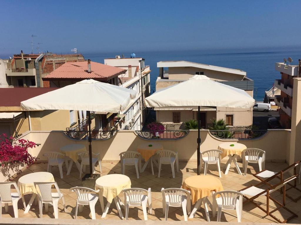 Terase ar baltām saulessargiem un galdiem, kas vērsta uz jūras skatu, fons ar pilsētas ēkām.