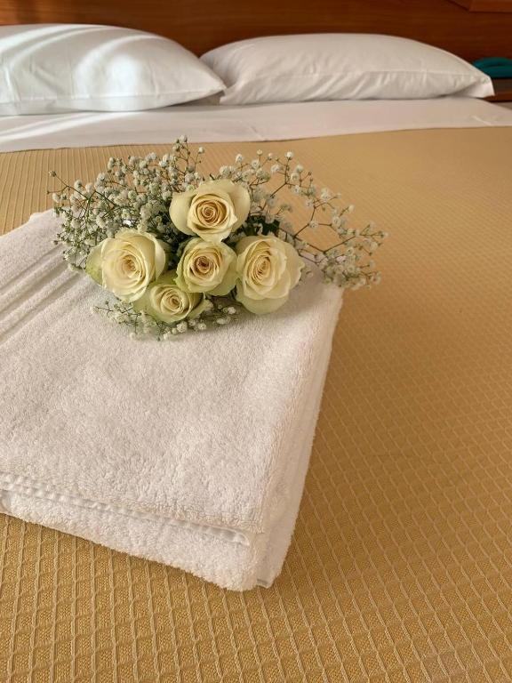 Skaista balto rožu pušķis, novietots uz salocīta baltas dvielītes, uz gultas ar dzeltenu pārklāju.