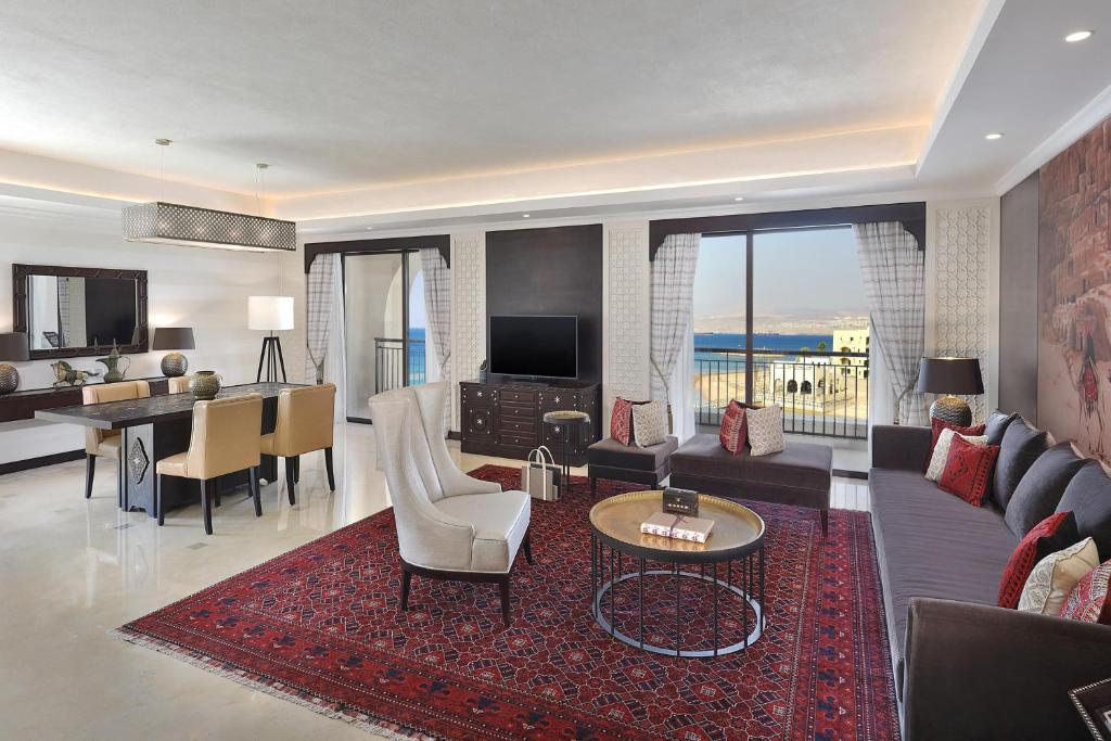 Eleganta viesistaba ar modernu interjeru, kas ietver mēbeles ar siltām krāsām, lielu logu ar skatu uz jūru un greznu paklāju. Ideāla vide relaksācijai un komfortam.