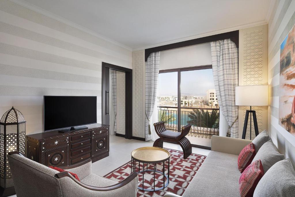 Mūsdienīgs viesnīcas numurs ar elegantu interjeru, kurā ir televizors, dīvāns un skaista skata uz ārpusi. Telpā ir arī dekoratīvi elementi un gaismas avots, kas veido mājīgu atmosfēru.