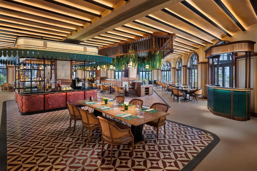 Elegants restorāna interjers ar izsmalcinātu apgaismojumu un modernu dizainu, kurā ir koka elementi un zaļumi. Vairāki galdi ar ērtām krēsliem ir izvietoti plašā telpā.