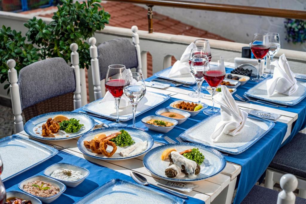 Skaista galda klāšana ar dažādām ēdienu porcijām un sarkano vīnu, kas pasniegts uz zila galda. Galda dekors papildina zaļumi un eleganta apkalpošana.