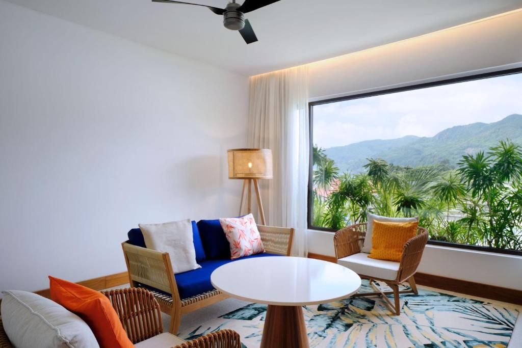 Mūsdienīgs dzīvojamās istabas interjers ar ērtu mēbeļu komplektu, kas sniedz skatu uz kalniem caur lielu logu. Telpa ir gaiša un gaumīgi iekārtota ar dabīgām krāsām un augiem.