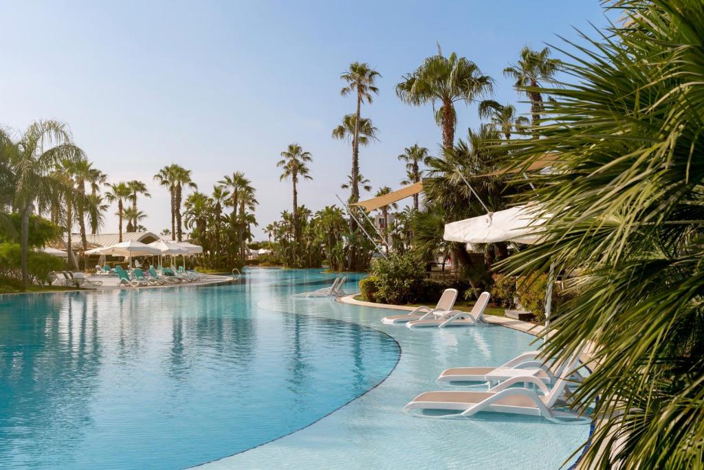 Susesi Luxury Resort baseina zona ar palmām un atpūtas krēsliem
