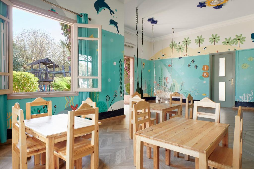 Gaiša un krāsaina bērnu istaba ar koka galdiem un krēsliem, ko ieskauj jūras un dabas motīvi. Logi paver skatu uz ārpusi, radot patīkamu un draudzīgu atmosfēru.