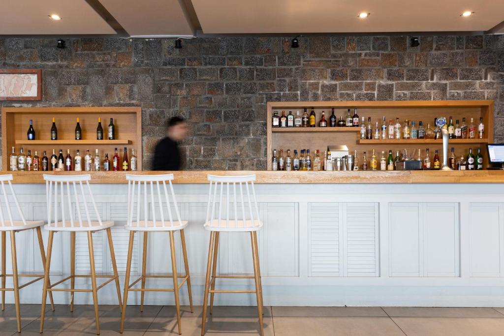 Mūsdienīgs bārs ar elegantu koka letes dizainu un dažādām alkoholiskajām dzērienu pudelēm. Fons ar akmens sienu piešķir telpai unikālu raksturu.