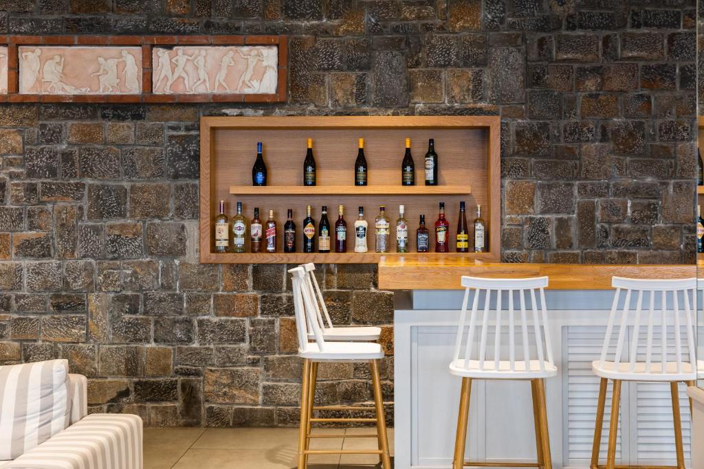 Mūsdienīgs bārs ar koka plauktu, uz kura izvietotas dažādas alkoholiskās dzērienu pudeles, un akmens sienu, kas rada siltu un aicinošu atmosfēru.