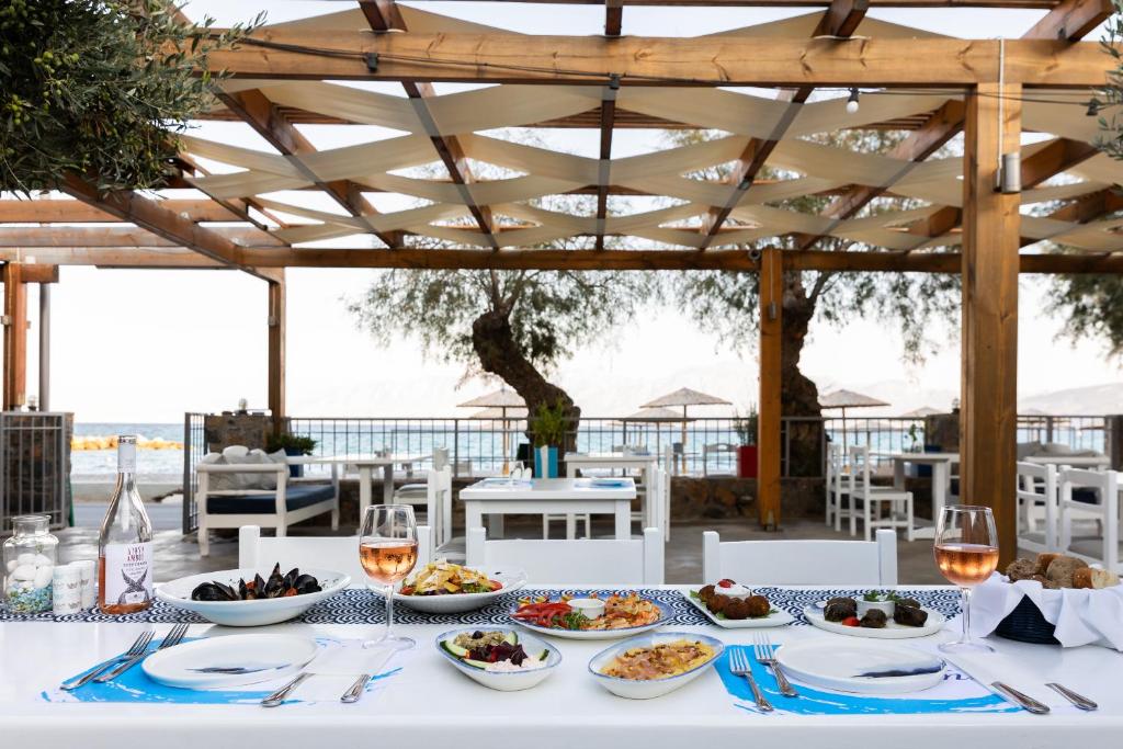 Elegantā restorāna terase ar skatu uz jūru, kur uz galda izvietoti dažādi gardi ēdieni un vīna glāzes. Ideāla atmosfēra relaksējošai maltītei.