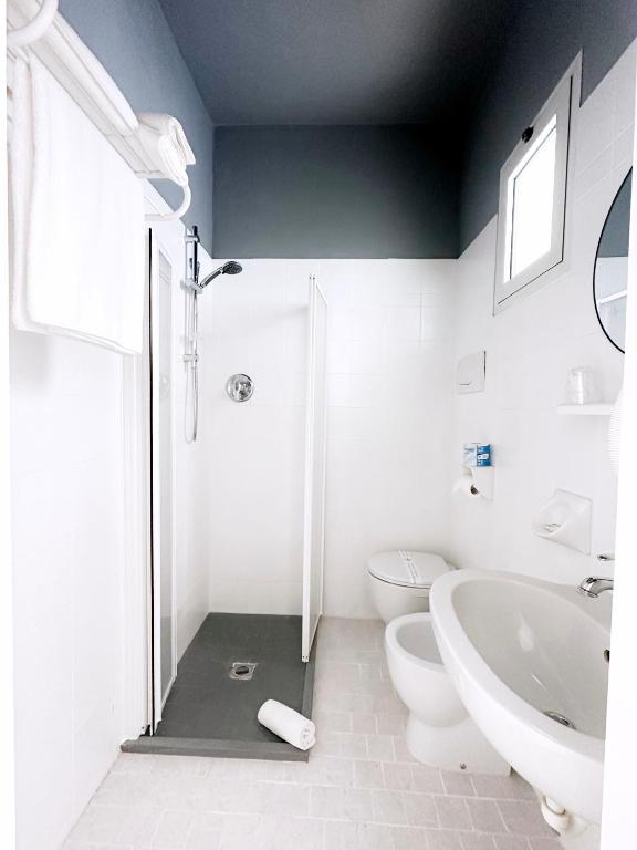 Mūsdienīgs vannas istabas interjers ar dušas kabīni, tualeti un izlietni, viss baltā un pelēkā krāsā. Telpa ir gaiša un tīra, ar minimālistisku dizainu.