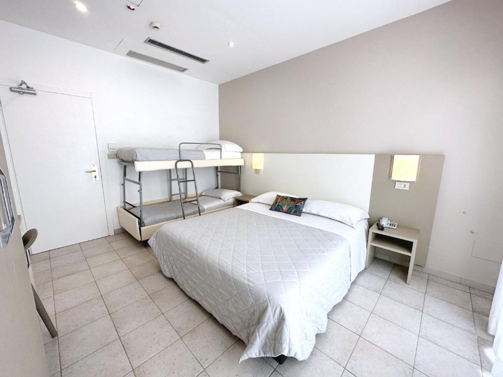 Mūsdienīga viesnīcas numuriņa iekārtojums ar divguļamo gultu un diviem bunkuru gultām. Telpa ir gaiša un vienkārša, ar flīžu grīdu un minimālu dekoru.