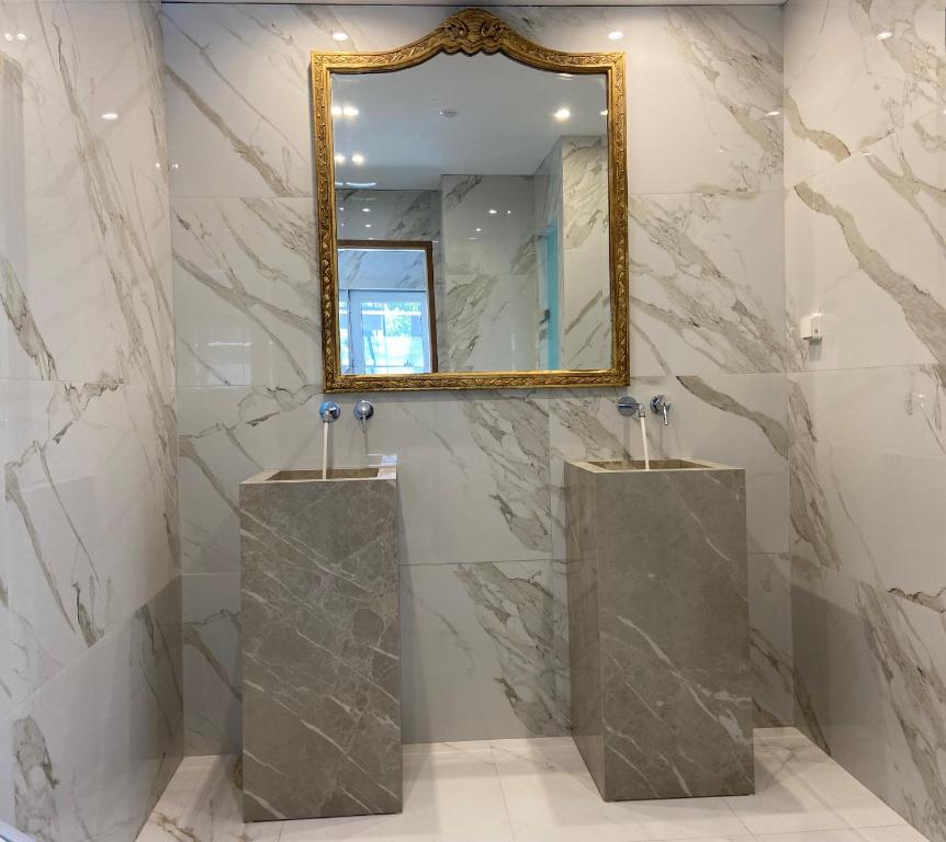 Moderns vannas istabas dizains ar diviem akmens izlietnēm un elegantu zelta spoguli uz marmora sienām.
