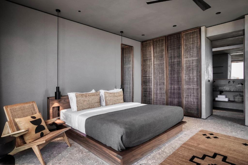 Mūsdienīga guļamistaba ar pelēku gultas veļu, rāmām un dabīgu apgaismojumu. Interjers apvieno minimalistisku dizainu ar dabīgām materiālu tekstūrām, radot mierīgu atmosfēru.