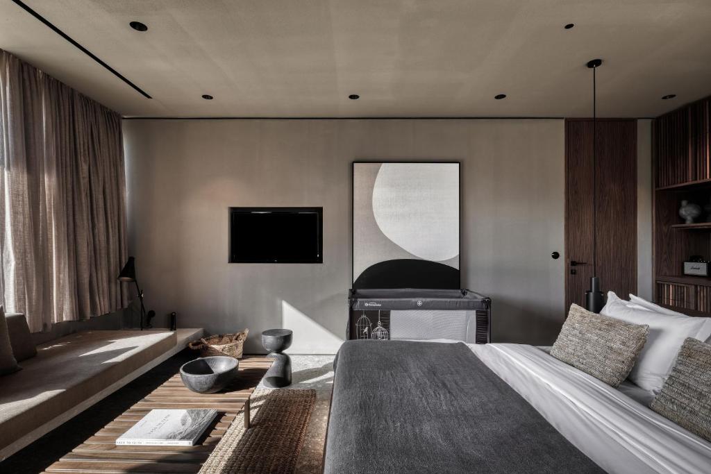 Mūsdienīgs guļamistabas interjers ar neitrālām krāsām, koka mēbelēm un mūsdienīgu mākslas darbu uz sienas. Telpā ir ērta gulta, saliekama dīvāna zona un televizors.