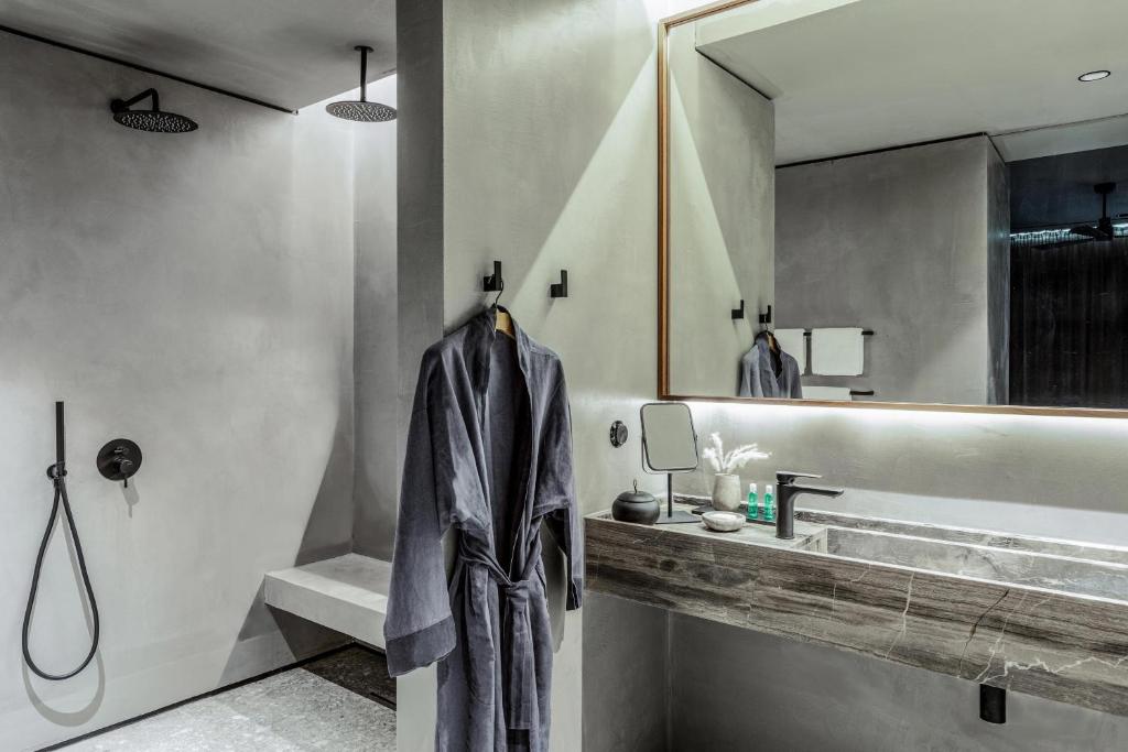 Mūsdienīgs vannas istabas interjers ar pelēkām sienām, elegantu izsmalcinātu izskatu un pelēku halātu, kas karājas uz āķa. Gaismas un spoguļi piešķir telpai plašumu un komfortu.