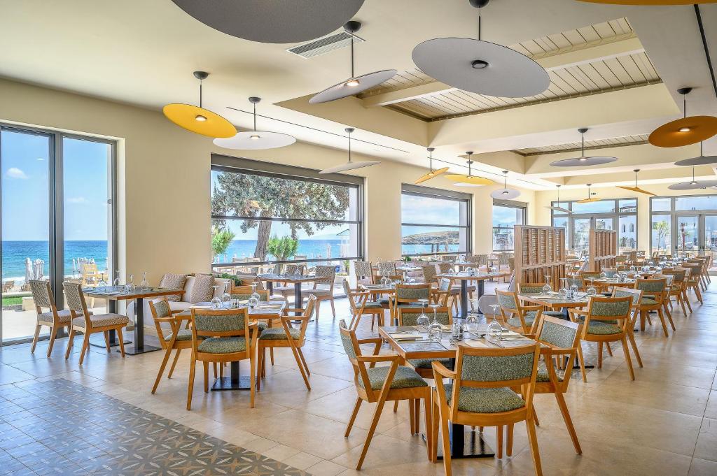 Moderns restorāns ar panorāmas skatu uz jūru, elegantām koka mēbelēm un gaišām krāsām. Telpa ir gaiša un plaša, radot patīkamu atmosfēru.