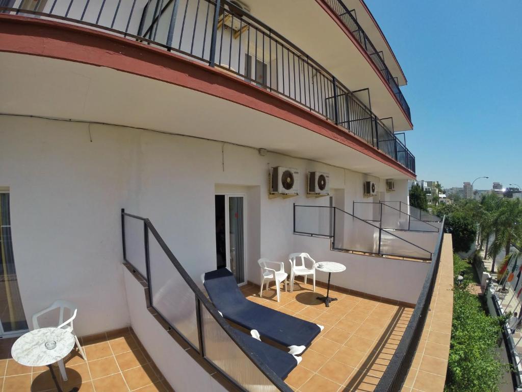 Balkons ar divām guļamvietām un galdiņu, ko ieskauj palmām un pilsētas ainava. Gaisa kondicionētāji uz sienas nodrošina komfortu karstās dienās.