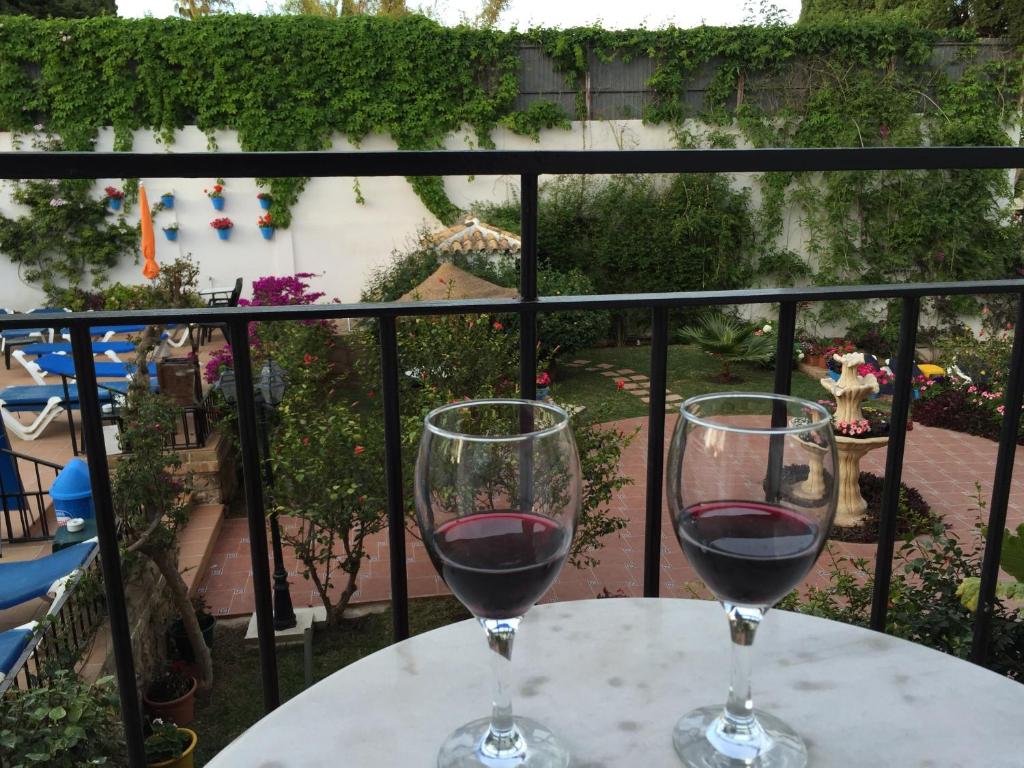 Divas vīna glāzes uz balta galda, fonā dārzs ar ziediem un baseinu. Viegla relaksācija ar skaistu ainavu.