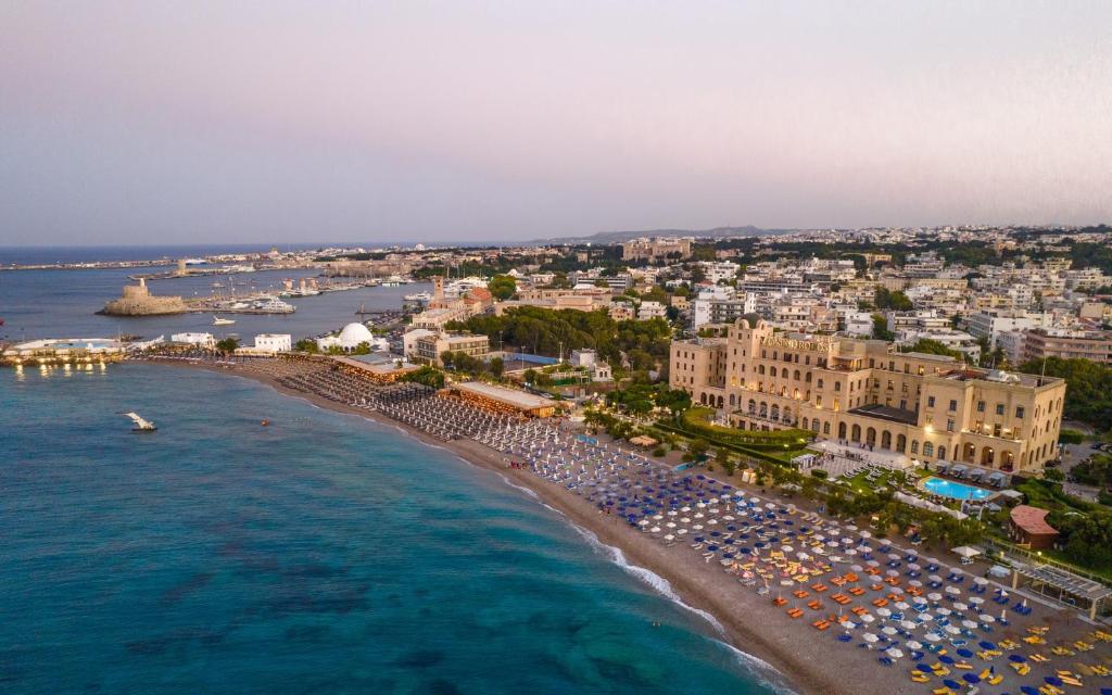 Skats uz Grande Albergo Delle Rose viesnīcu piekrastē ar pludmali un pilsētu fona.