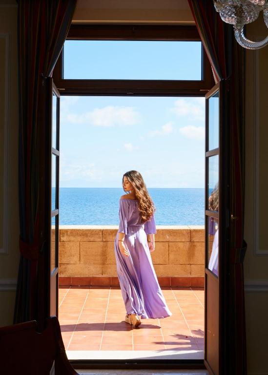 Jauna sieviete violetā kleitā skata uz jūru no Grande Albergo Delle Rose