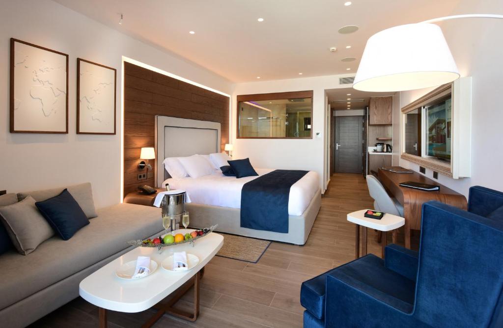 Mūsdienīgs viesnīcas numurs ar elegantu interjeru, kurā ir liela gulta, dīvāns un moderns rakstāmgalds. Telpā ir arī augļu grozs un eleganta apgaismojuma sistēma.