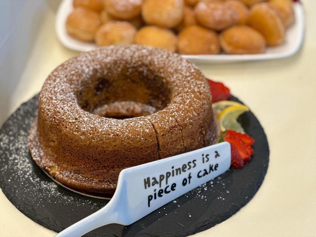 Šokolādes kūka ar cukura pūderi un uzrakstu "Happiness is a piece of cake", pasniegta uz melnas akmens plāksnes, blakus redzami saldumi.