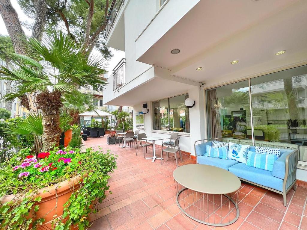 Mūsdienīgs āra terases dizains ar ziediem, palmām un ērtām mēbelēm, ideāls relaksācijai. Terase ir plaša un gaiša, veidojot patīkamu atmosfēru.