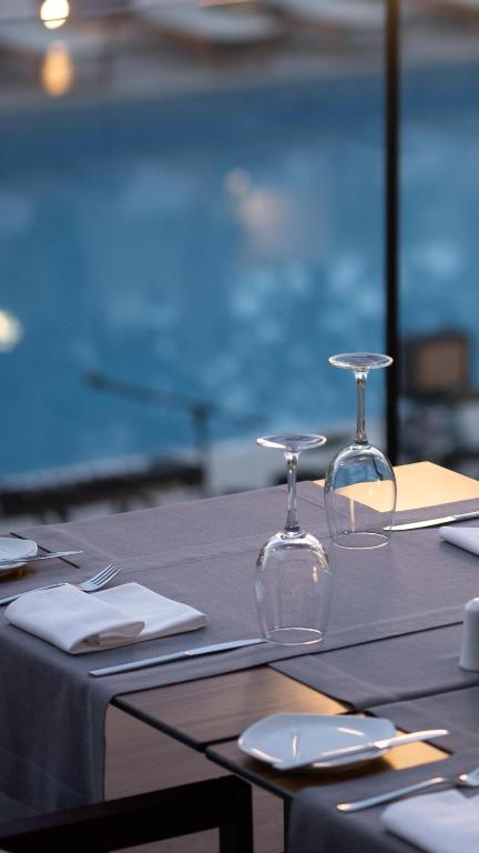 Elegants restorāna galdiņš ar glāzēm un traukiem, kas atrodas blakus baseinam. Mierīga atmosfēra un skaista ainava veido ideālu vietu maltītei.