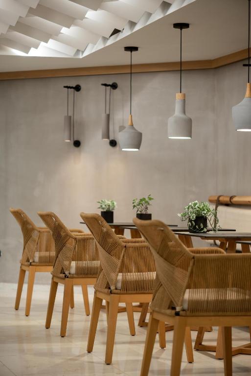 Mūsdienīgs interjers ar koka krēsliem un stilīgām gaismas ķermeņiem, kas rada siltu un viesmīlīgu atmosfēru. Galda virsma rotāta ar augiem, piešķirot telpai dzīvīgumu.