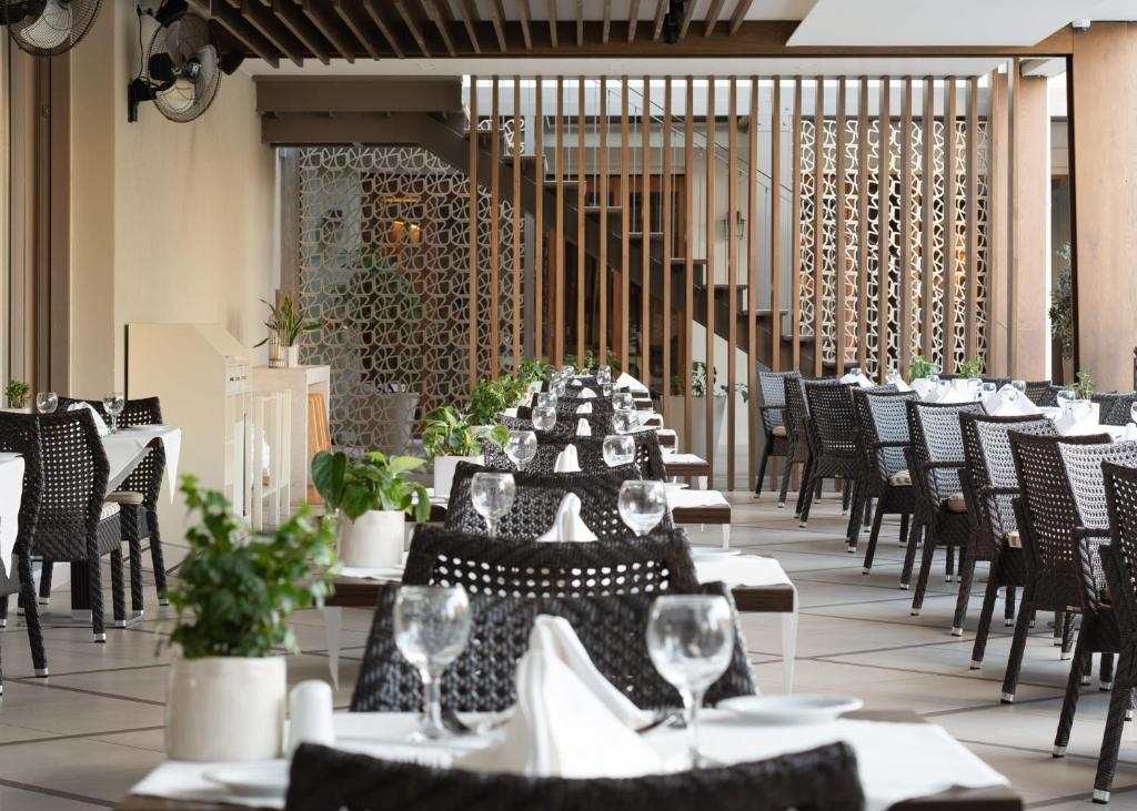 Mūsdienīgs restorāns ar elegantiem galdiem, melnām krēsliem un zaļiem augiem, radot patīkamu atmosfēru. Interjers ar koka akcentiem un dekoratīvām sienām piešķir telpai stilīgu izskatu.