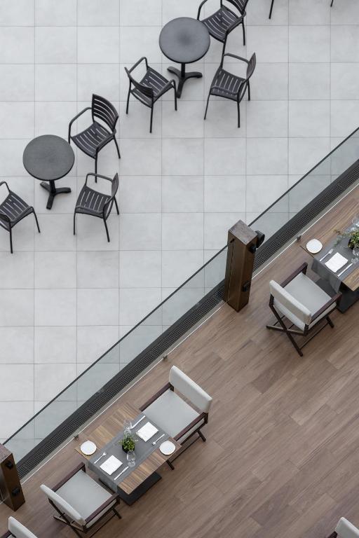 Mūsdienīga kafejnīca ar stilīgu dizainu, baltiem galdautiem un koka mēbelēm, kurā redzami tukši galdi un krēsli.