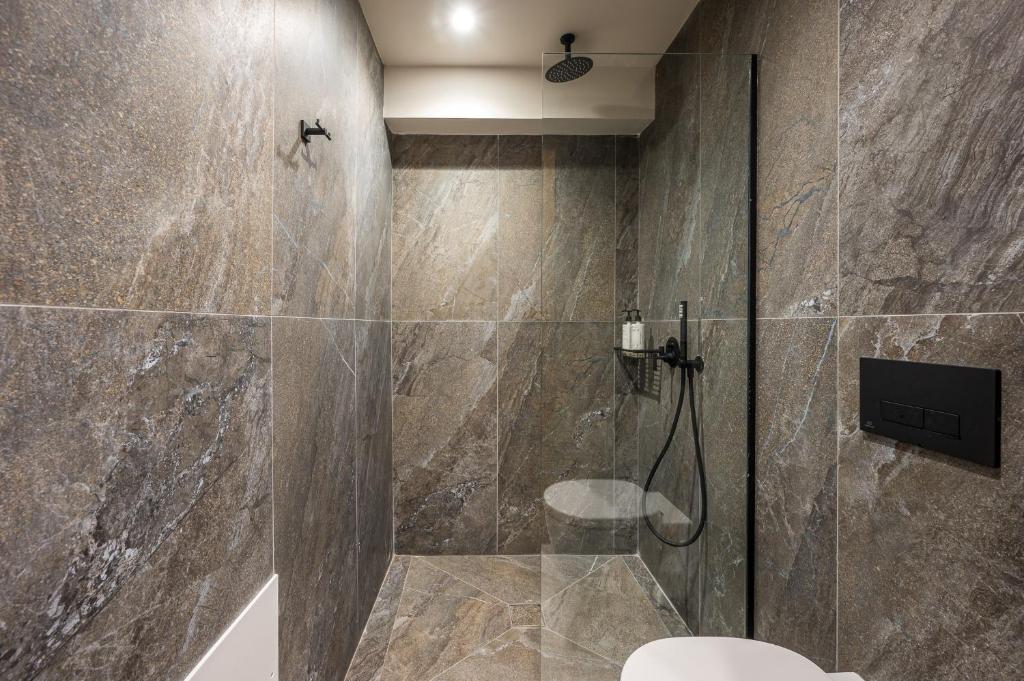 Mūsdienīga dušas telpa ar akmens izskata flīzēm, stikla durvīm un melniem sanitārajiem elementiem. Elegants un minimālisma dizains, kas rada relaksējošu atmosfēru.