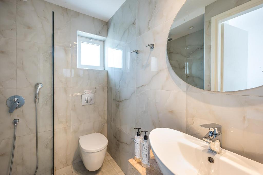 Mūsdienīgs un elegants vannas istabas interjers ar marmora apdari, dušas kabīni un apaļu spoguli. Šajā telpā ir arī gaiši toņi un dabīgā apgaismojuma elementi.