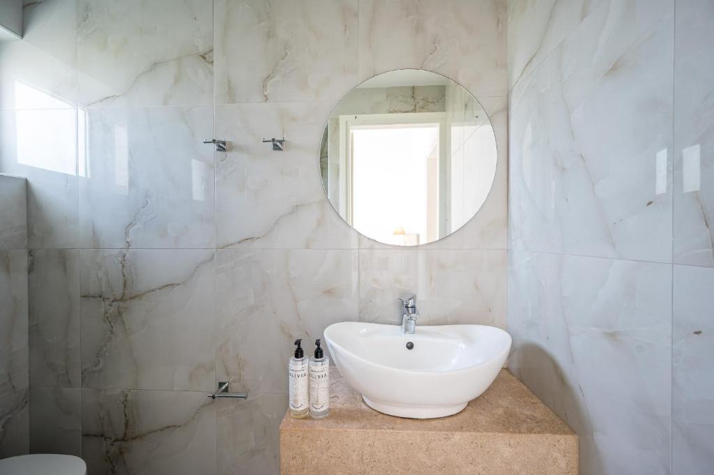 Mūsdienīgs vannas istabas interjers ar marmora efektu, apaļu spoguli un stilīgu izlietni. Uz plaukta redzami higiēnas līdzekļi.